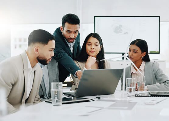 A group of professionals having a focused meeting around a table, looking at a laptop, symbolizing business and IT consulting services, strategic discussions, and collaborative planning.