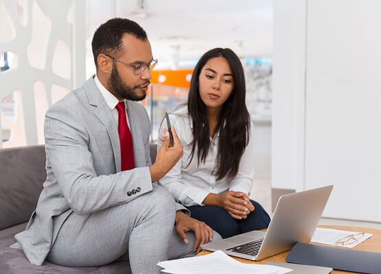 Two professionals discussing a project over a laptop, with one holding a cup, symbolizing consulting services and collaborative strategy sessions.