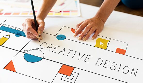 A hand writing "CREATIVE DESIGN" on paper surrounded by design tools, symbolizing the focus on design education and creativity.