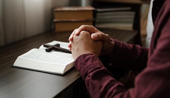 A person reading a book or making notes at a table in a dimly lit, quiet setting, symbolizing the spiritual nature of the service.