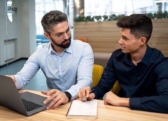 Two business professionals in casual attire having a focused discussion and shaking hands, symbolizing a successful partnership and consulting engagement.