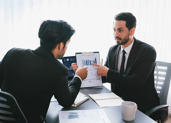 Two business professionals shaking hands across a table, symbolizing a successful partnership, agreement, or consulting engagement.